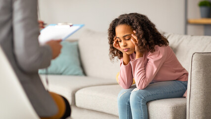 Unhappy girl listening to psychologist at meeting. Doctor consulting stressed teen at counselling...