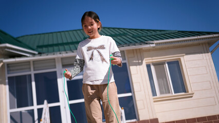 Funny smiling girl jumps rope on the background of her house. The teenager is enjoying what is happening. Active outdoor activities © chekart