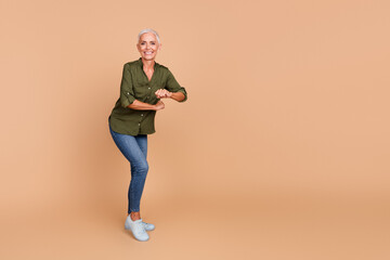Smiling mature woman in casual attire posing confidently on a beige backdrop, showing energy and happiness in a relaxed, stylish manner