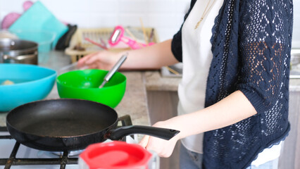 Close-up of a woman about to fry pancakes in a pan on a gas stove. Mom cooks something delicious in...