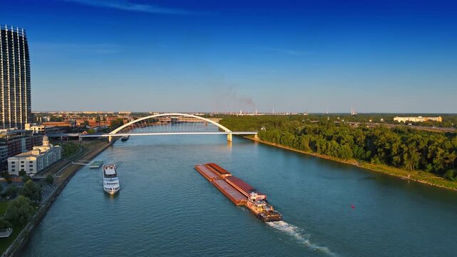Barge pushing the loads by the Danube towards the Appolo Bridge. Riverboat travel along the shore. Aerial view. Bratislava, Slovakia.