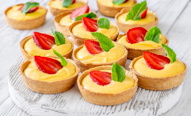 Mini mango cream tarts with strawberry and mint on white wooden board
