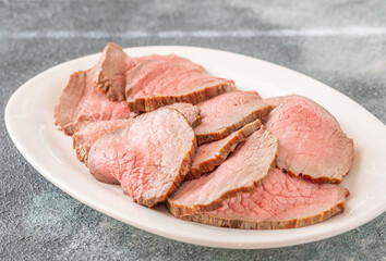 Perfectly sliced roast beef medium rare with seared crust on white plate