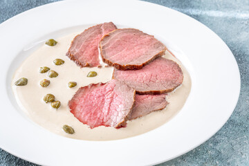 Elegant Vitello Tonnato with scattered capers and creamy sauce on plate