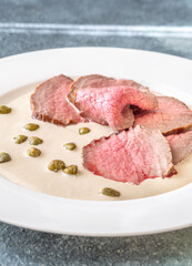 Elegant Vitello Tonnato with scattered capers and creamy sauce on plate
