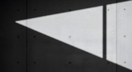 A stark concrete wall is bisected by an acute triangle of light and shadow, casting an austere mood that highlights the material's texture and geometry in minimalist composition for striking effect.
