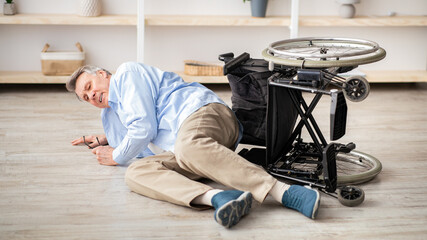Senior man with physical disability lying on floor after falling down from his wheelchair at home....