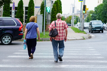 Elderly couple crossing pedestrian lines on a city street during an afternoon walk in summer