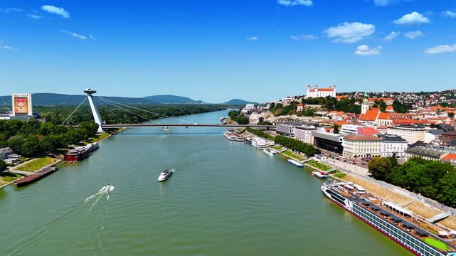 Boats and riverboats moving by the Danube River near the UFO Bridge. Aerial perspective on the beautiful cityscape of the old town in Bratislava, Slovakia.