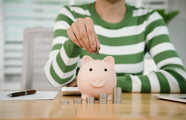 A person calculates finances while saving money, placing coins into a piggy bank. The scene symbolizes budgeting, investment, financial planning, and building future wealth with responsibility and dis
