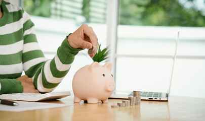 A person calculates finances while saving money, placing coins into a piggy bank. The scene...