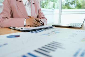 A business professional analyzing financial charts and graphs with a pen, calculator, and laptop, focusing on economic data, growth reports, corporate strategy, management planning, and decision-makin