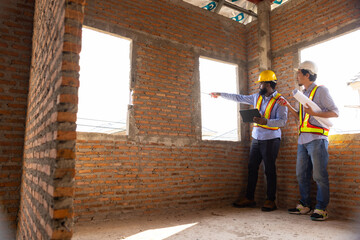 Fototapeta premium Working Engineering construction : African American construction worker Architects and japanese contractor working together at building under construction site. Engineering in safety harthat helmet