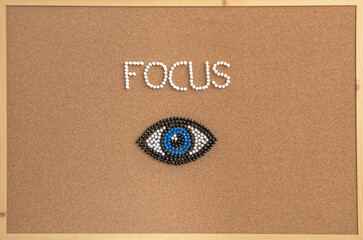 Creative conceptual image of the word "FOCUS" and an eye symbol arranged with colorful push pins on a cork bulletin board. Represents concentration, mindfulness, clarity, vision, and motivation.