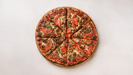 Top view of whole baked pizza with cheese, sausage, tomatoes, mushrooms and herbs on a wooden board. Light neutral background, minimal food styling.