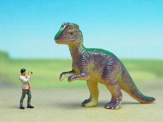 Fototapeta premium Mini toy of action figure at table with blurred background. Miniature photography concept design. Minifigure of photographer, animal and dinosaurs character at nature. Adventure at wild life with dino