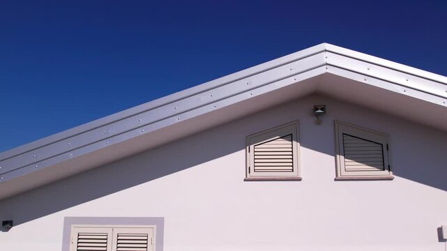 A plumber installed aluminum gutters and aluminum-colored downspouts on a newly built home with a tile roof. The areas of the roof without gutters were finished with aluminum cornice trim.