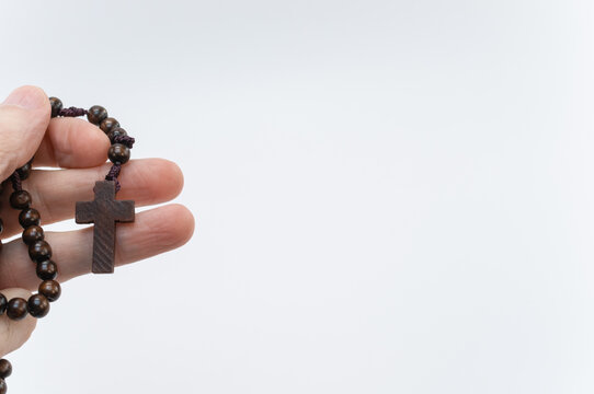 una mano in primo piano che impugna un rosario in legno scuro con una piccola croce pendente, sfondo bianco con spazio vuoto
