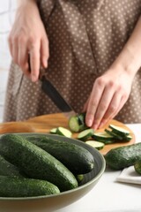 Woman cutting fresh cucumber at white table, closeup