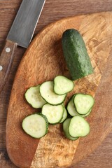 Slices of fresh cucumber and knife on wooden table, flat lay
