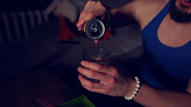 Closeup view of man pouring sparkling lemonade from the can into transparent glass filmed in slow motion. Caucasian male person is watching television at night time in the darkness and having soda
