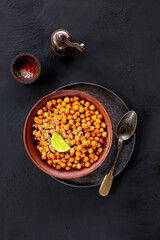 Vegetarian food. Roasted chickpeas with spices and lime in a bowl on black background top view vertical photo