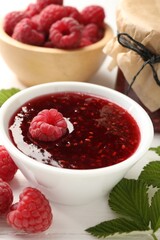 Sweet raspberry jam, berries and green leaves on table, closeup