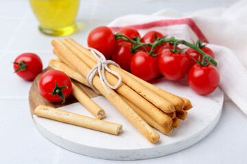 Delicious grissini sticks and fresh tomatoes on white table, closeup