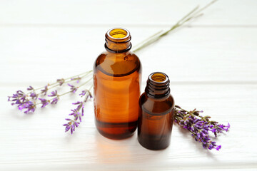 Lavender essential oil and flowers on white wooden table, closeup
