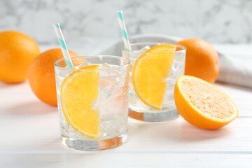Sparkling water with orange slices in glasses and fresh fruits on white wooden table, closeup