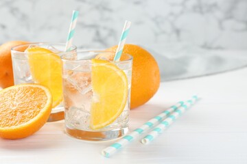 Sparkling water with orange slices in glasses and fresh fruits on white wooden table, closeup. Space for text