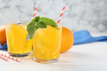 Refreshing soda water with orange slices in glasses, mint and fresh fruits on white wooden table, closeup