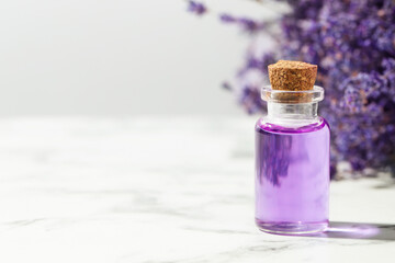 Lavender essential oil in bottle on white marble table against light grey background, closeup. Space for text