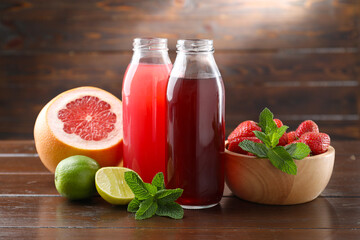Tasty juices in glass bottles, fresh fruits, strawberries and mint on wooden table