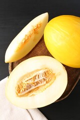 Cut and whole ripe melons on black wooden table, flat lay