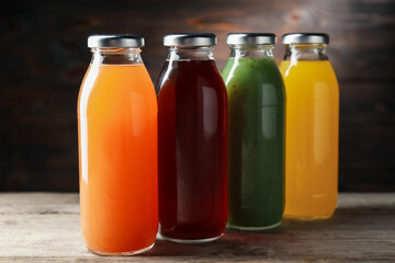 Tasty juices in glass bottles on wooden table against brown background, closeup