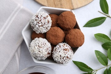 Delicious homemade candies with cocoa powder and coconut flakes in bowl on white table, flat lay