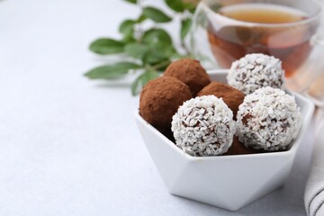 Delicious homemade candies with cocoa powder and coconut flakes in bowl on white table, closeup. Space for text