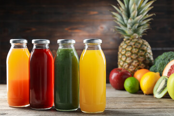 Tasty juices in glass bottles and fresh ingredients on wooden table against brown background, closeup
