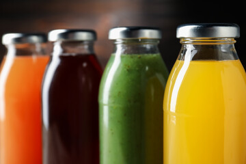 Tasty juices in glass bottles on blurred brown background, closeup