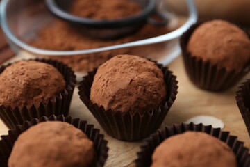 Delicious homemade candies powdered with cocoa on wooden table, closeup