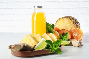 Tasty juice in glass bottle, fresh fruits, ginger and mint on white table against brick wall, closeup