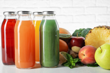 Tasty juices in glass bottles and ingredients on white table against brick wall, closeup