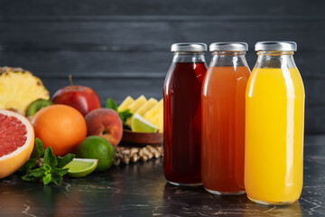 Tasty juices in glass bottles, fresh fruits and mint on black marble table, closeup