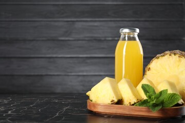 Tasty juice in glass bottle, pineapple and mint on black marble table, closeup. Space for text