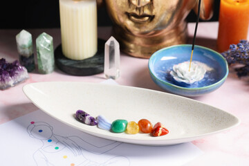 Chakra gemstones, incense and human body drawing on light pink table, closeup
