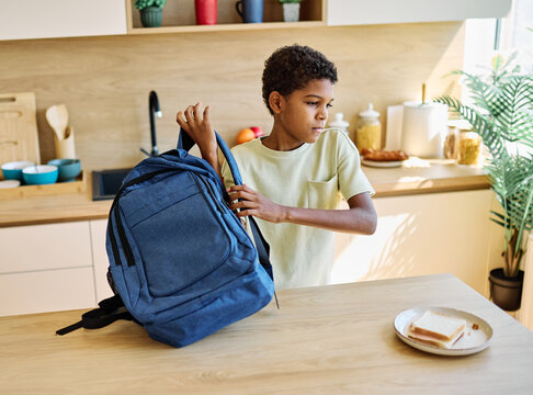 Portret of  a black teen boy with a school backpack having fun alone preparing sanwiches snack for  breakfast and school  in kitchen - Powered by Adobe