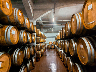 Many oak barrels for storing wine or whiskey stacked in dark cellar. Winery production process and aging concept. Big round wine cellar for storage of alcoholic beverages placed inside modern factory
