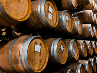 Many oak barrels for storing wine or whiskey stacked in dark cellar. Winery production process and aging concept. Big round wine cellar for storage of alcoholic beverages placed inside modern factory