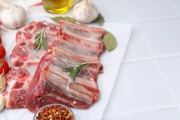 Fresh raw beef ribs and spices on white tiled table, closeup. Space for text